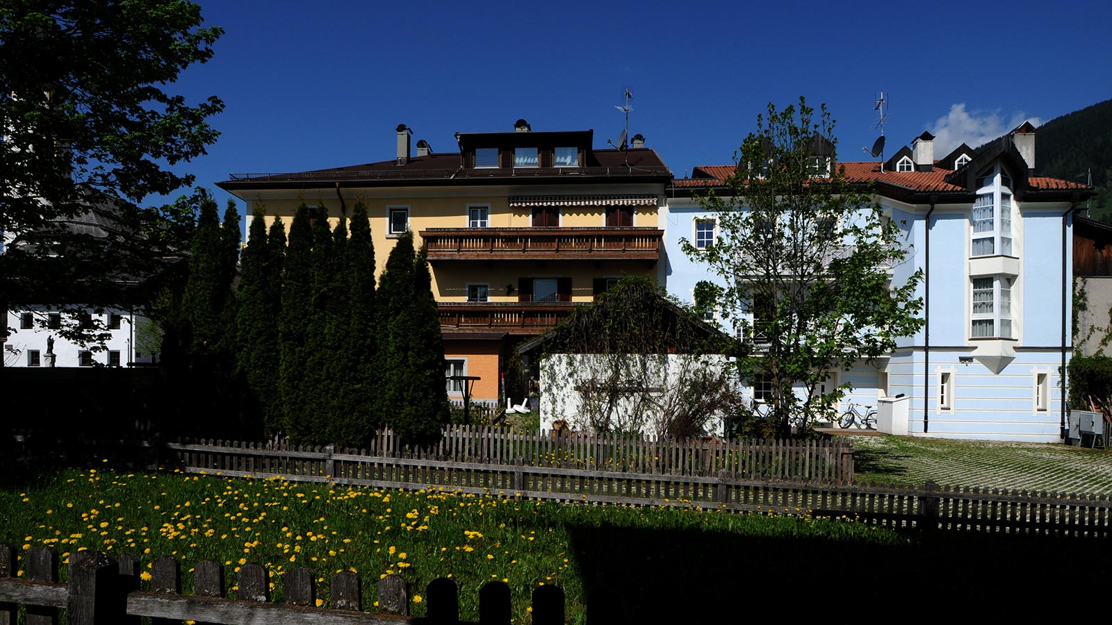 Blick aus dem Garten auf die gelben und blauen Wohnungen der Villa Christina, darunter ein mit Holzzäunen eingefasster Innenhof.