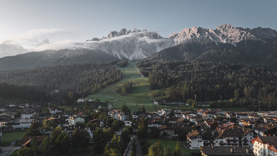 Panorama di San Candido al tramonto con piste verdi e Dolomiti avvolte da leggere nuvole