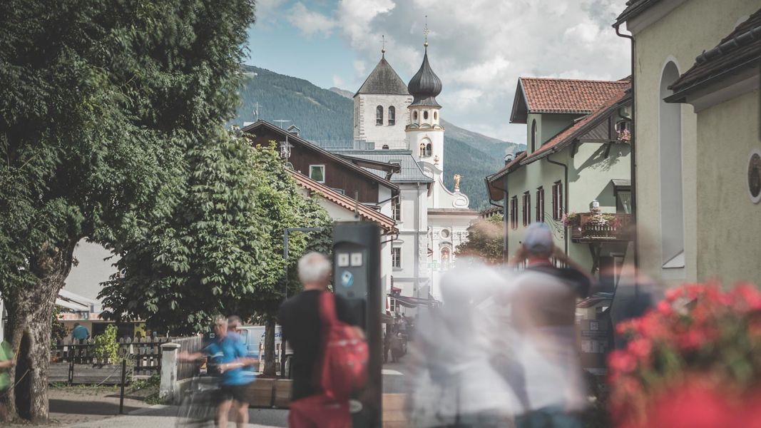 Veduta del centro di San Candido con la chiesa parrocchiale sullo sfondo e persone che passeggiano