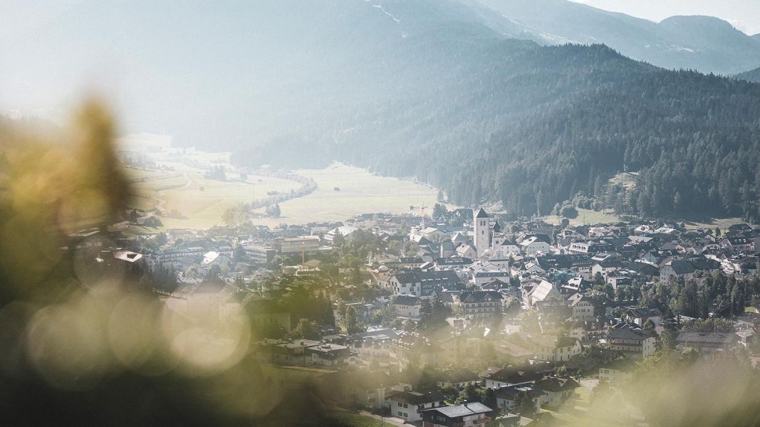 Vista dall’alto su San Candido immersa nella valle con montagne boscose sullo sfondo
