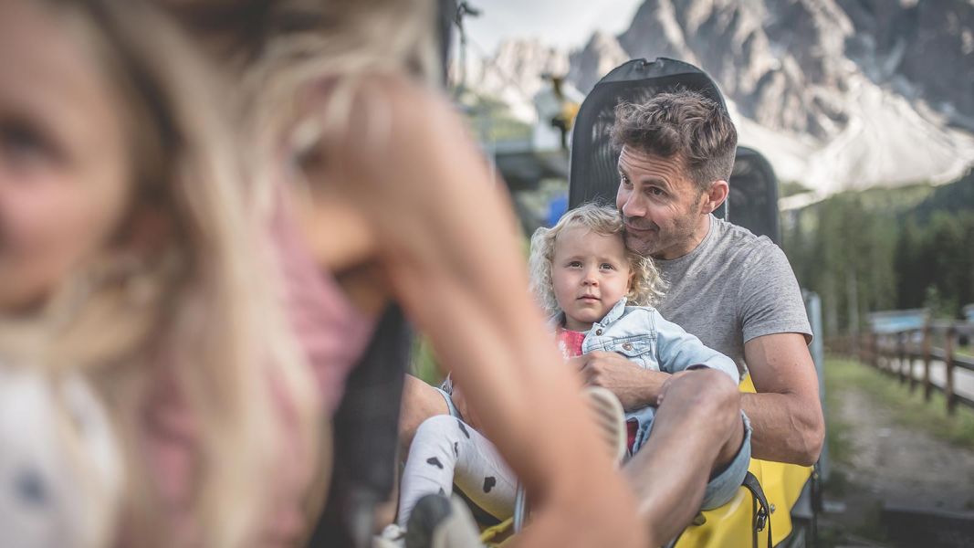 Padre e figlia seduti su un bob estivo ai piedi delle Dolomiti