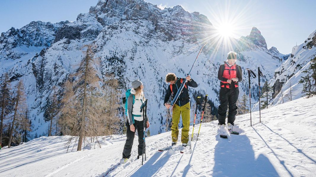 Gruppo di amici che prepara l’attrezzatura da sci alpinismo in una vallata innevata con il sole basso