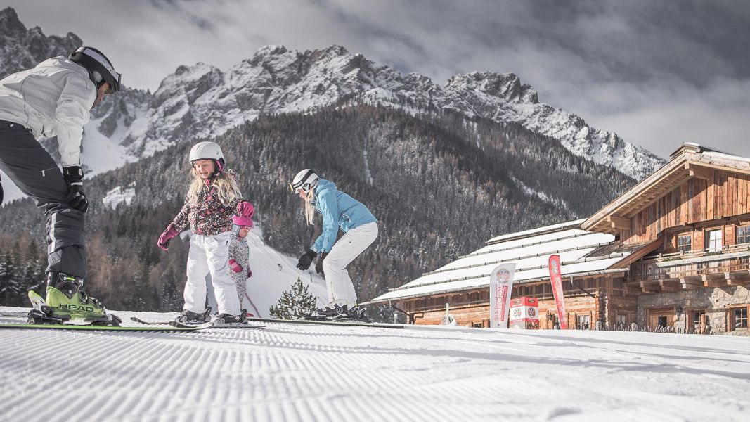 Bambini che imparano a sciare davanti a una baita di montagna con le Dolomiti innevate sullo sfondo