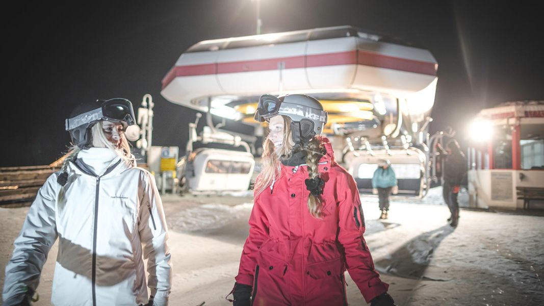 Sciatori che escono da una cabinovia illuminata durante una serata di sci notturno