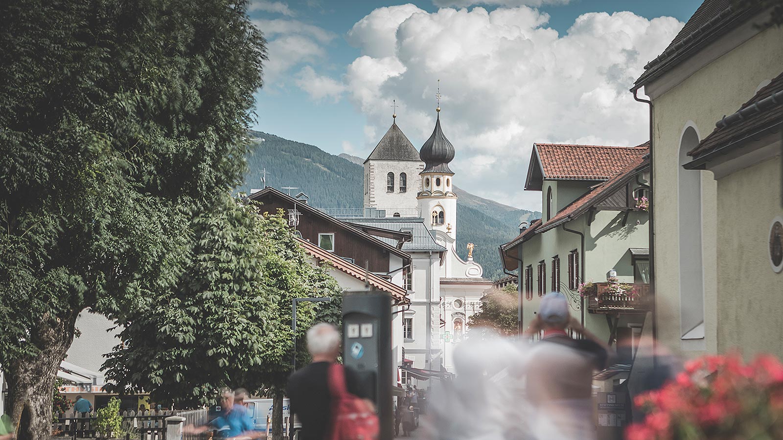Touristen und Bürger von Innichen schlendern durch die Straßen des Dorfes, vor der Kirche San Michele.